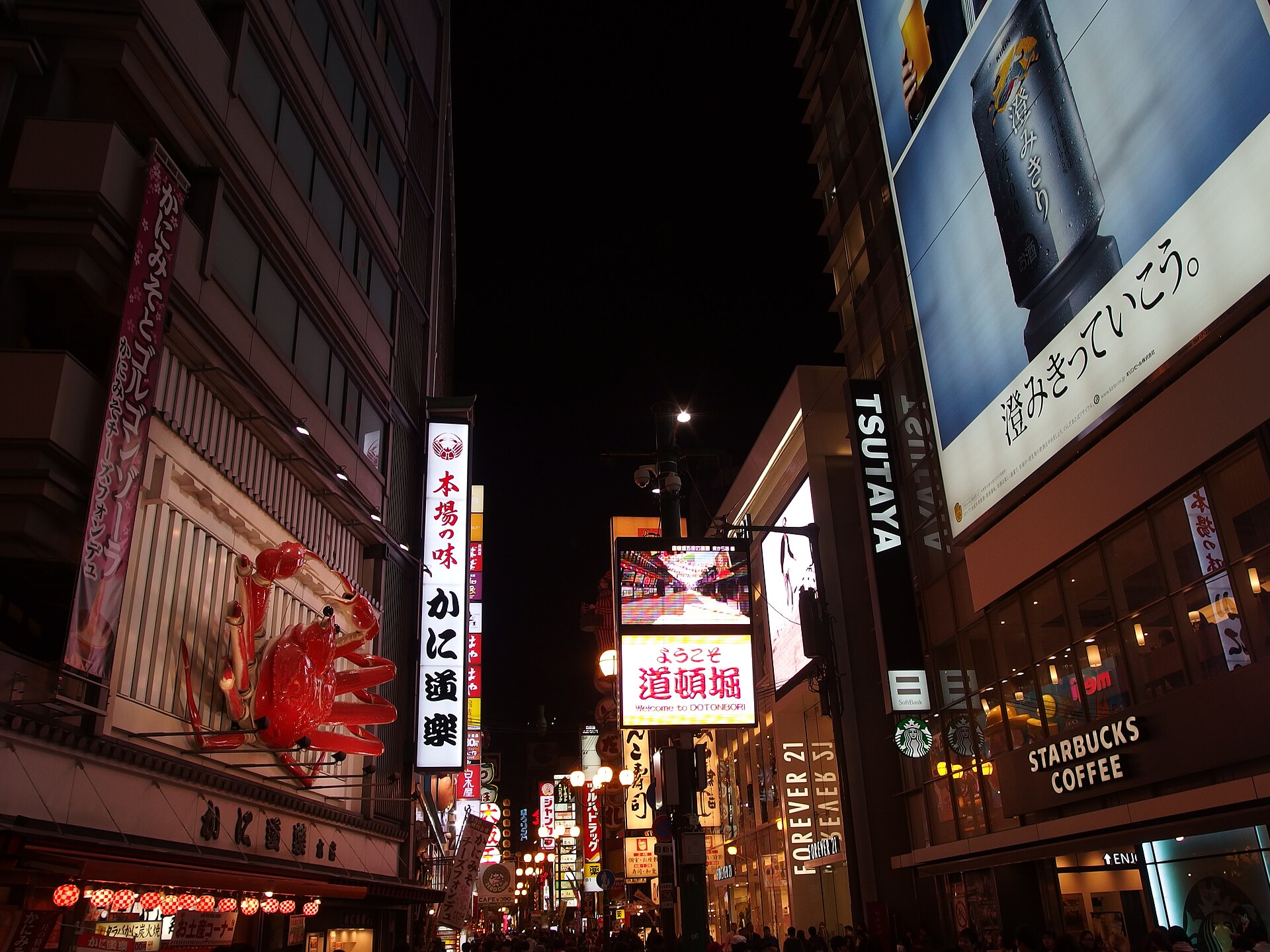 ถนนในย่านโดทงโบริ โอซาก้า ยามค่ำที่มีป้ายไฟ ร้านค้า และคนเดิน