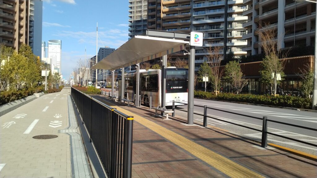 รถ Tokyo BRT จอดที่ป้ายฮารุมิฟูโตะพาร์ก มีอาคาร HARUMI FLAG อยู่ด้านหลัง