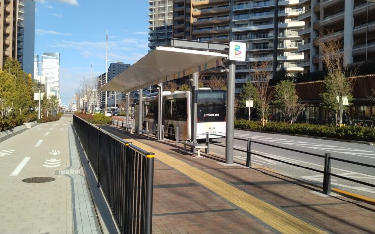 รถ Tokyo BRT จอดที่ป้ายฮารุมิฟูโตะพาร์ก มีอาคาร HARUMI FLAG อยู่ด้านหลัง