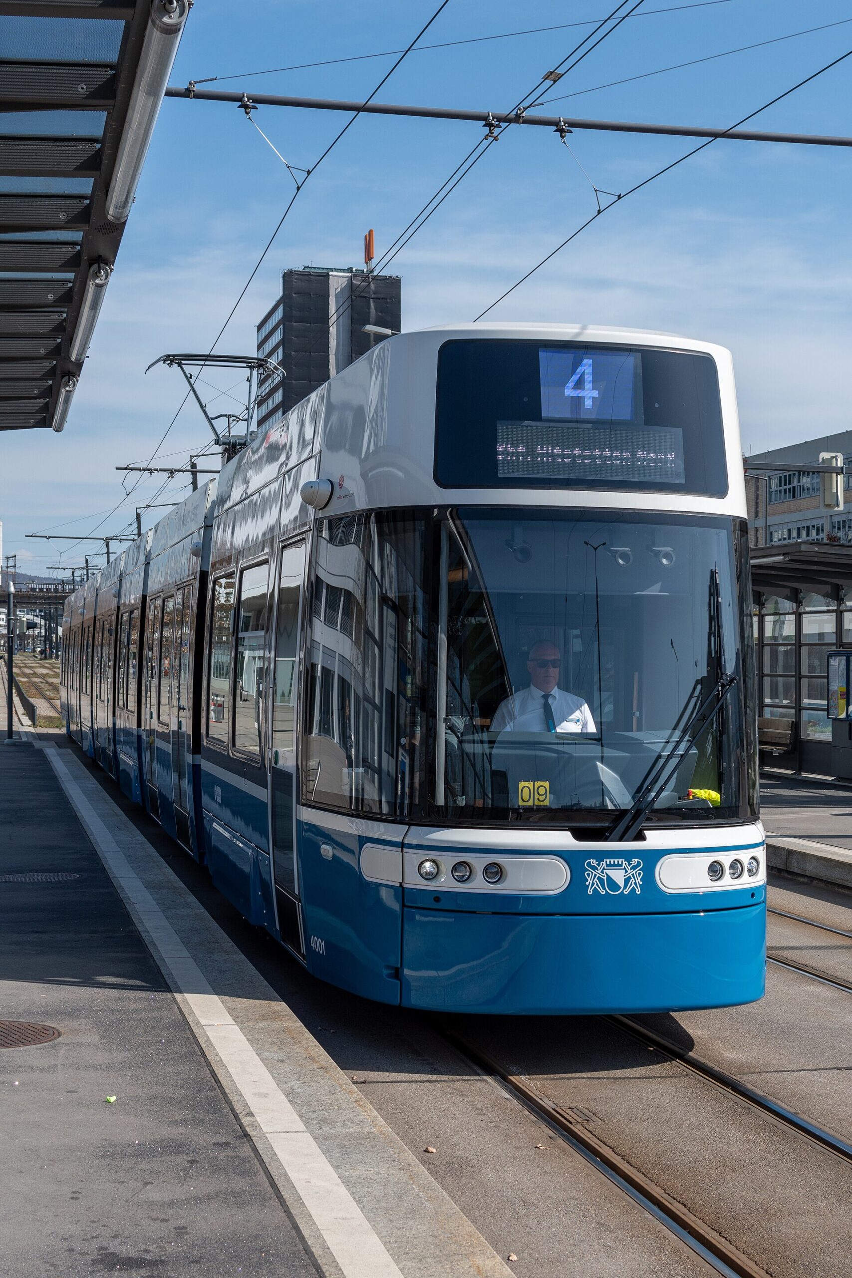 รถราง Flexity สีน้ำเงินขาวของซูริกจอดที่ชานชาลาในเวลากลางวัน
