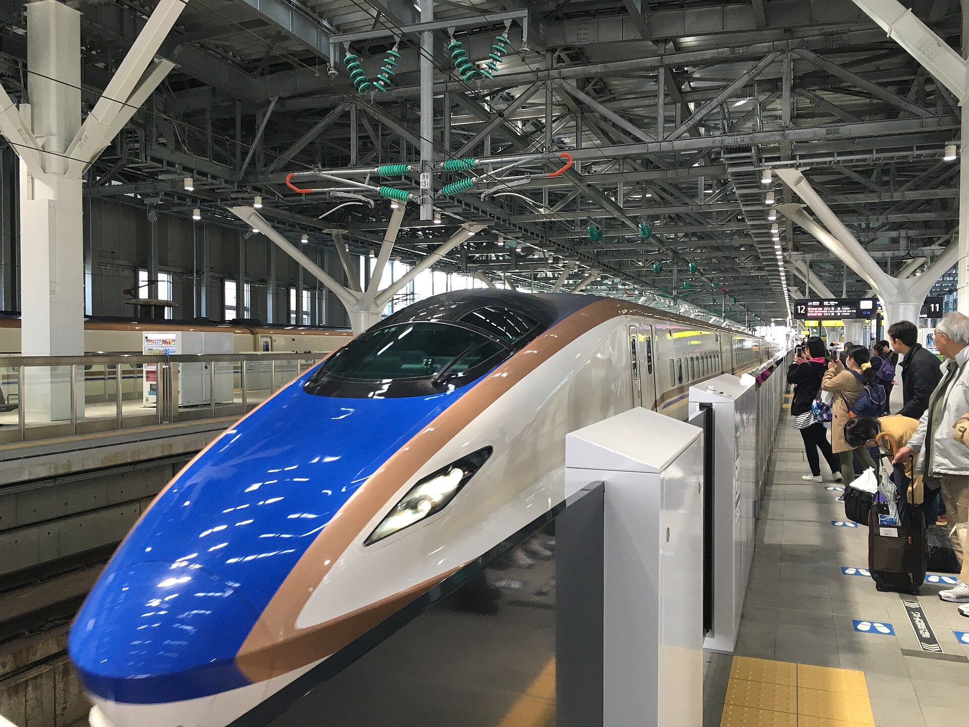 รถไฟ Hokuriku Shinkansen E7 สีน้ำเงินจอดที่ชานชาลาสถานี Toyama