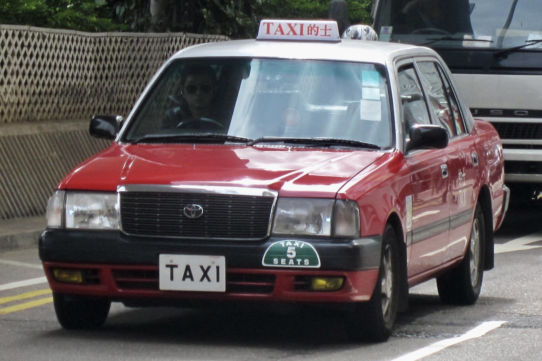 แท็กซี่ Urban Taxi สีแดงของฮ่องกงบนถนนในเวลากลางวัน