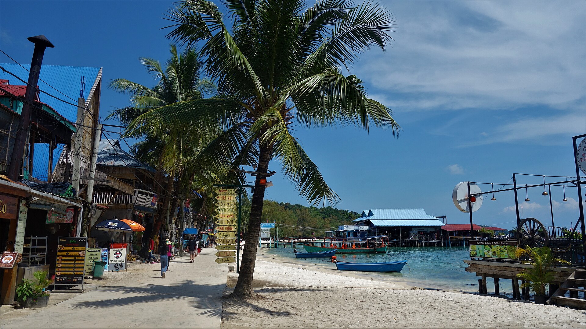 ริมน้ำเกาะรง มีต้นมะพร้าว เรือ และอาคารริมชายหาด