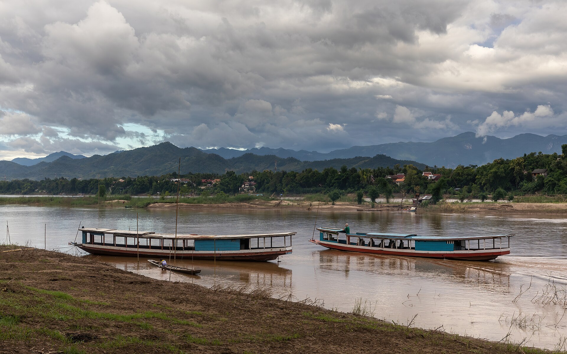 เรือบนแม่น้ำโขงที่หลวงพระบางช่วงบ่าย มีภูเขาและฟ้าครึ้ม
