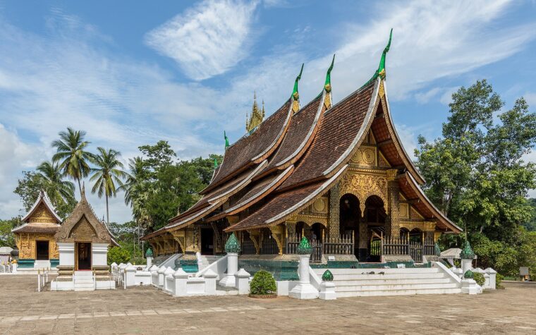 วัดเชียงทองหลวงพระบาง หลังคาสีหลายชั้นและหน้าบันทองในลานหินใต้ฟ้าสีฟ้า